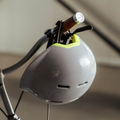 Grijze fietshelm die aan het stuur van een fiets hangt. Fluo striping, ventilatiegaten en reflecterende body.