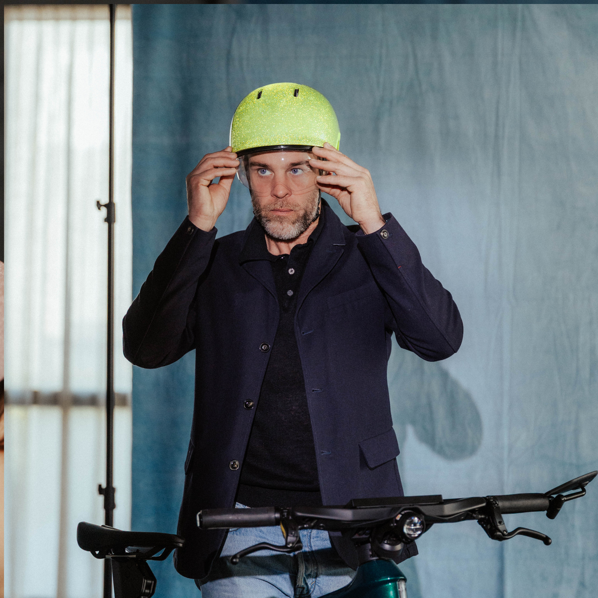 Een man die zijn gele fietshelm rechtzet terwijl hij voor een fiets staat, met op de achtergrond een blauwe muur.